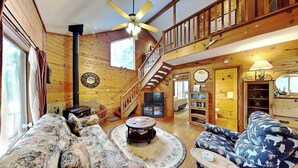A log cabin interior with a staircase, a fireplace, a television, and a bookshelf. - Moose Manor by Ruidoso Vacation Rentals (Ruidoso)