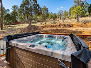 A hot tub on an outdoor deck with a wooden floor, surrounded by trees and a clear sky.