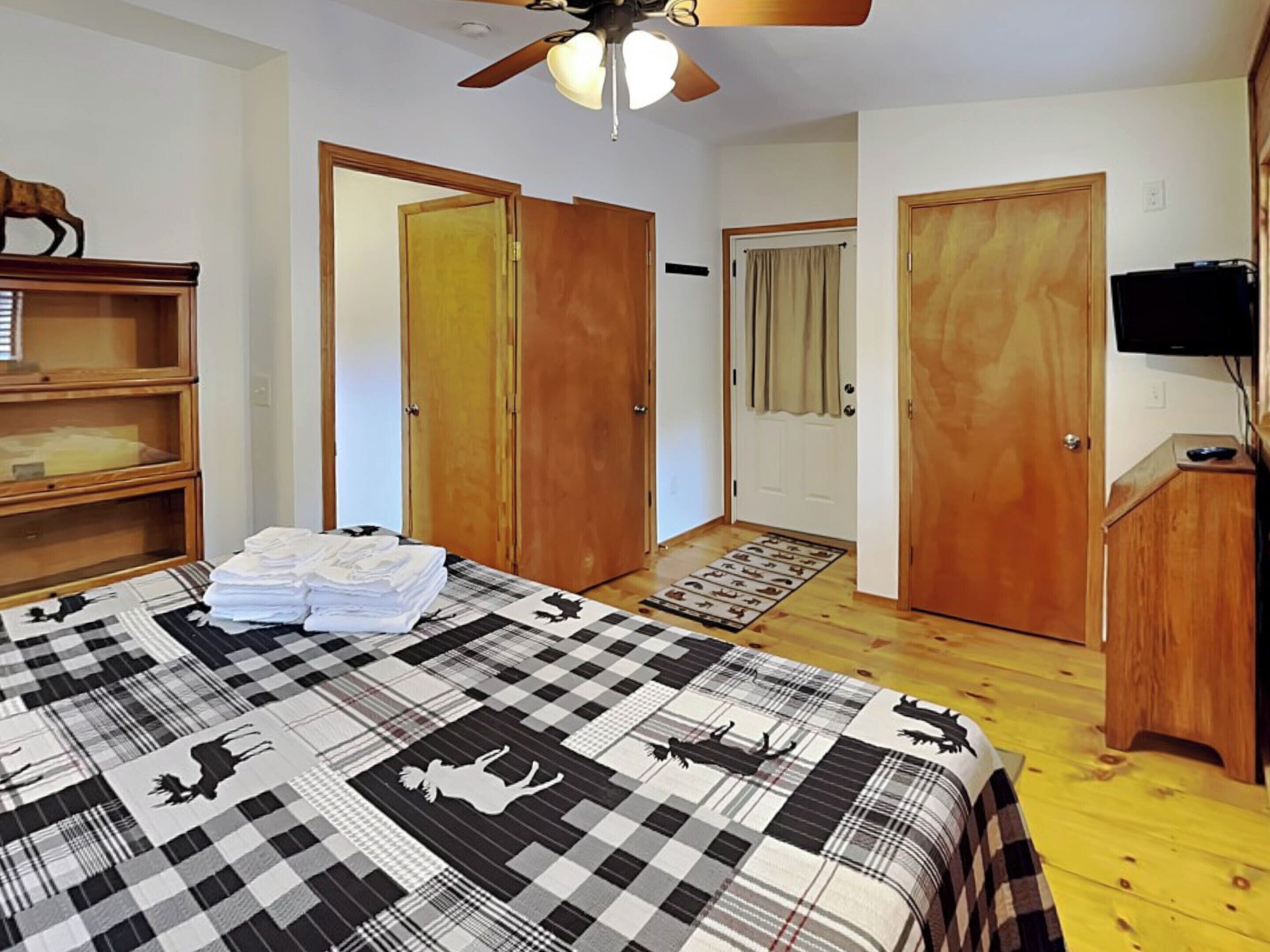 A bedroom with a bed, wooden wardrobe, a television, and a ceiling fan.