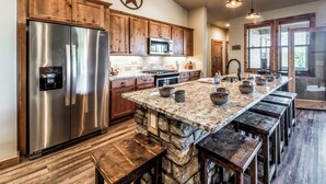 A kitchen with a large island, wooden cabinets, a stainless steel refrigerator, and a stone accent wall.