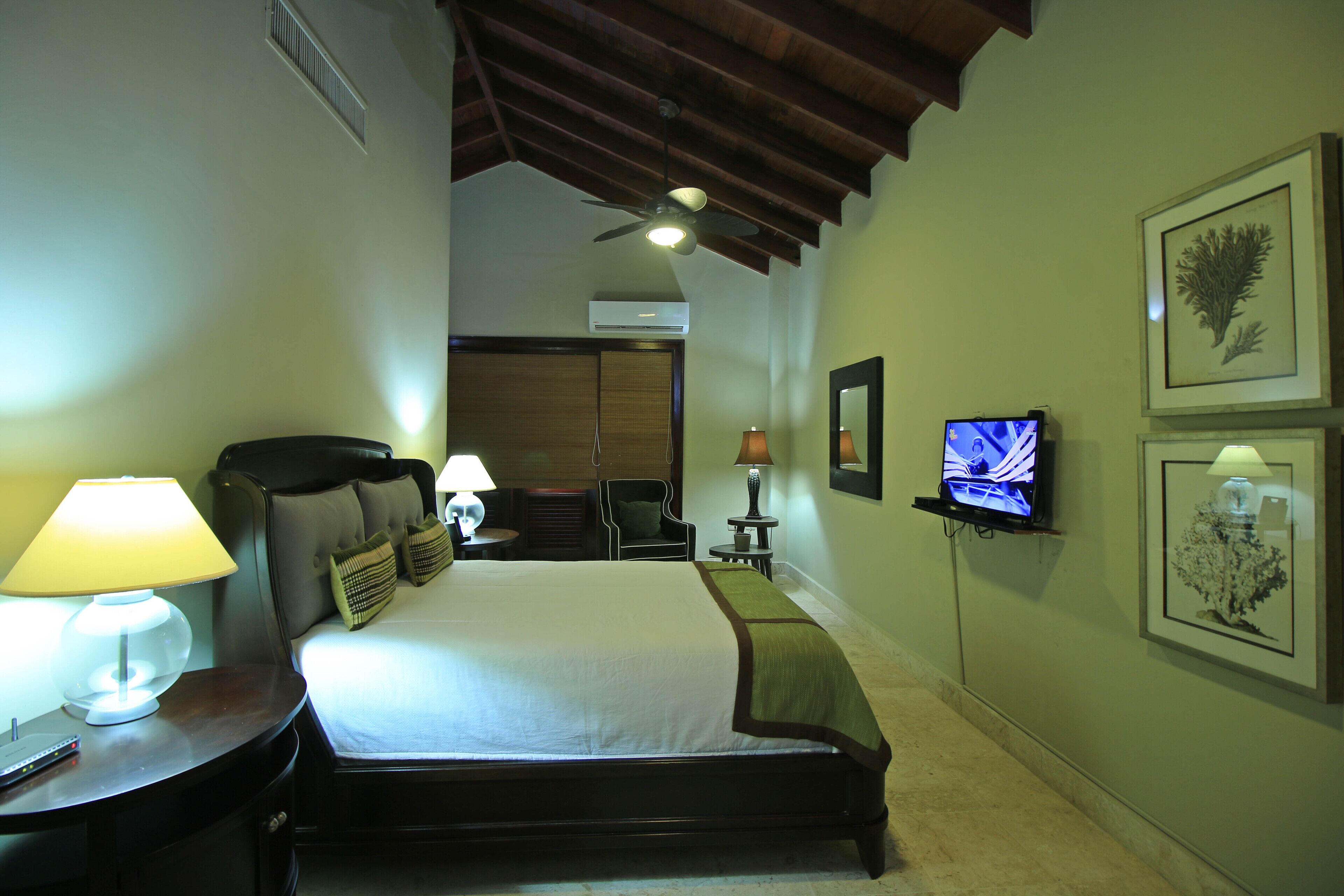 Een hotelkamer met een groot bed, een plafondventilator, een televisie en kunstwerken in lijsten aan de muur.