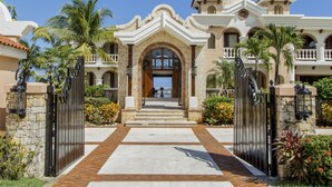 Una entrada imponente con un camino de entrada porticado que conduce a un edificio de estilo mediterráneo, con arcos y un balcón con barandilla.