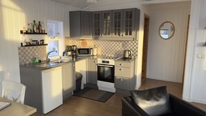Une cuisine compacte équipée d’un évier, d’une cuisinière et d’un four à micro-ondes. Un petit coin repas est aménagé avec une table et une chaise.