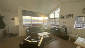 Un salon comprenant un canapé, des fauteuils et une table basse. De grandes fenêtres offrent une vue sur le paysage.