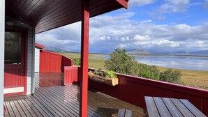 Une terrasse en bois avec des rampes rouges, d’où l’on peut admirer un lac et des montagnes.