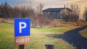 Un panneau de signalisation bleu indiquant un espace de stationnement, avec un poteau en bois et le mot « VISITEUR » écrit en dessous.
