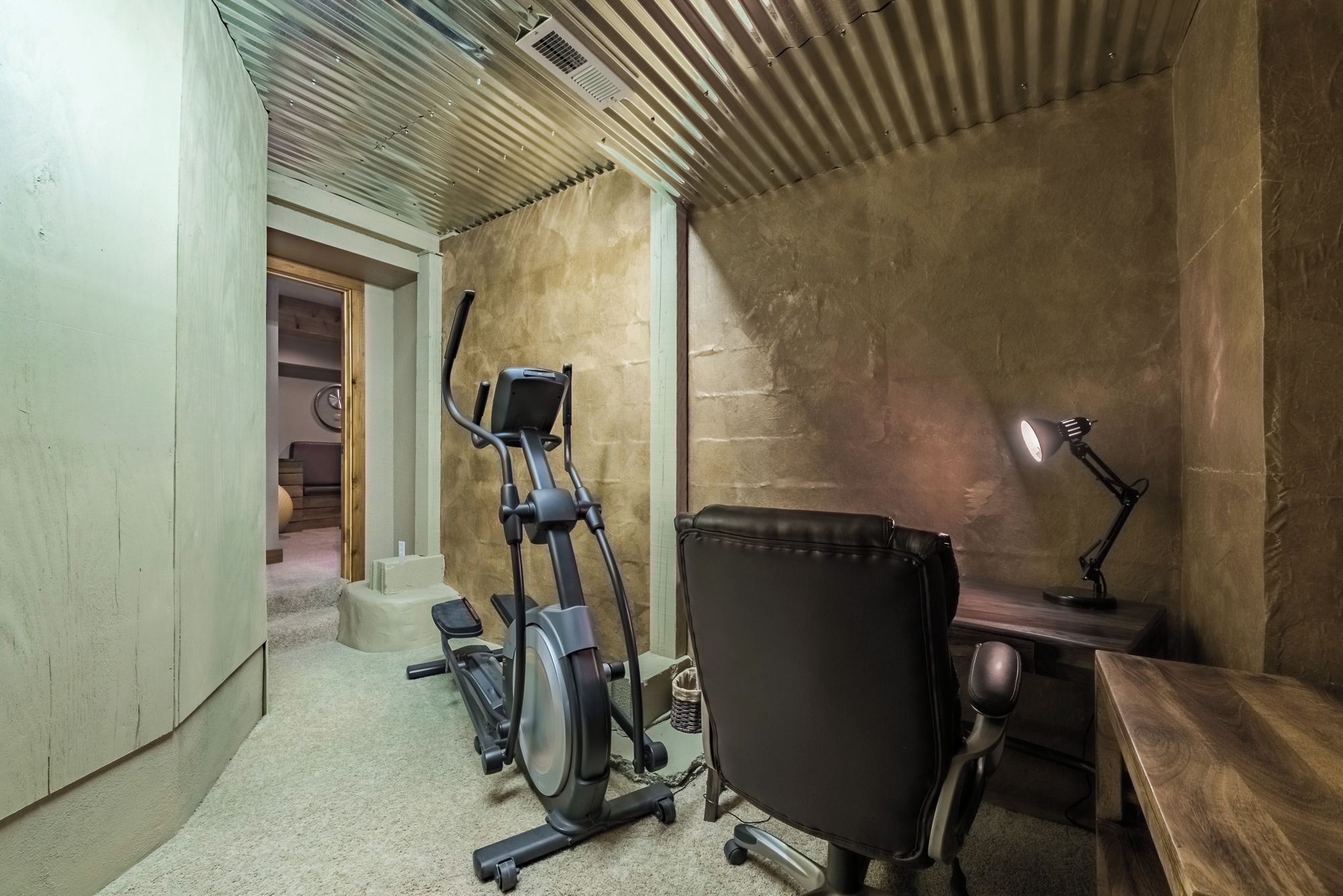 Ein Zimmer mit Laufband, Bürostuhl, Schreibtisch, Lampe und einem kleinen Tisch.