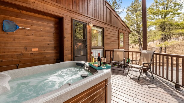 A wooden cabin with a hot tub on the deck, a chair, and a table. - High Loop by Ruidoso Vacation Rentals (Ruidoso)