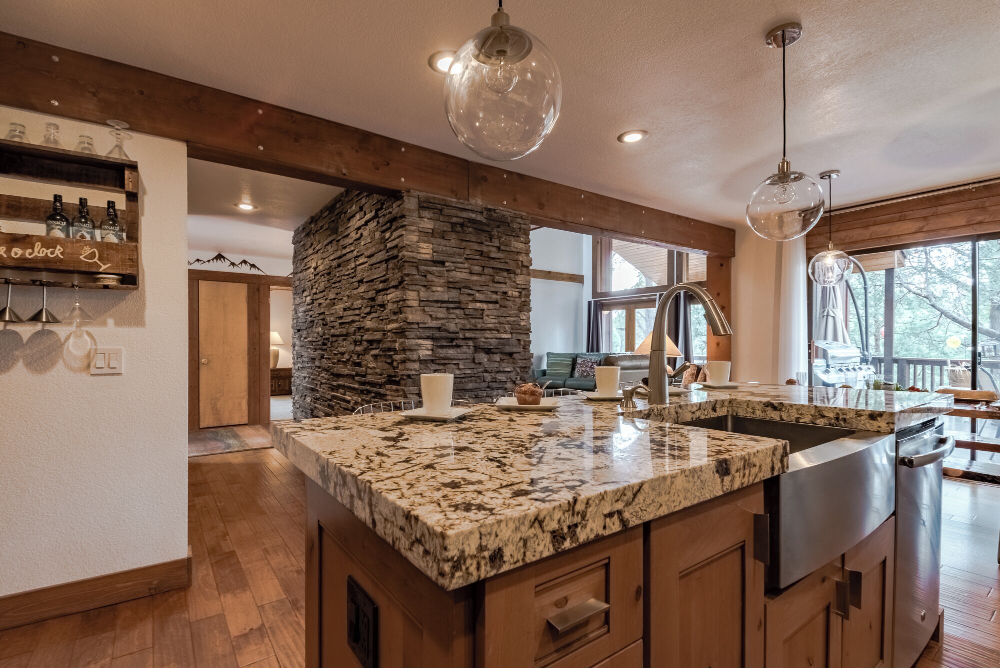 A kitchen with a large granite island, wooden cabinets, a stone accent wall, and pendant lighting.