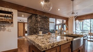 A kitchen with a large granite island, wooden cabinets, a stone accent wall, and pendant lighting. - High Loop by Ruidoso Vacation Rentals (Ruidoso)
