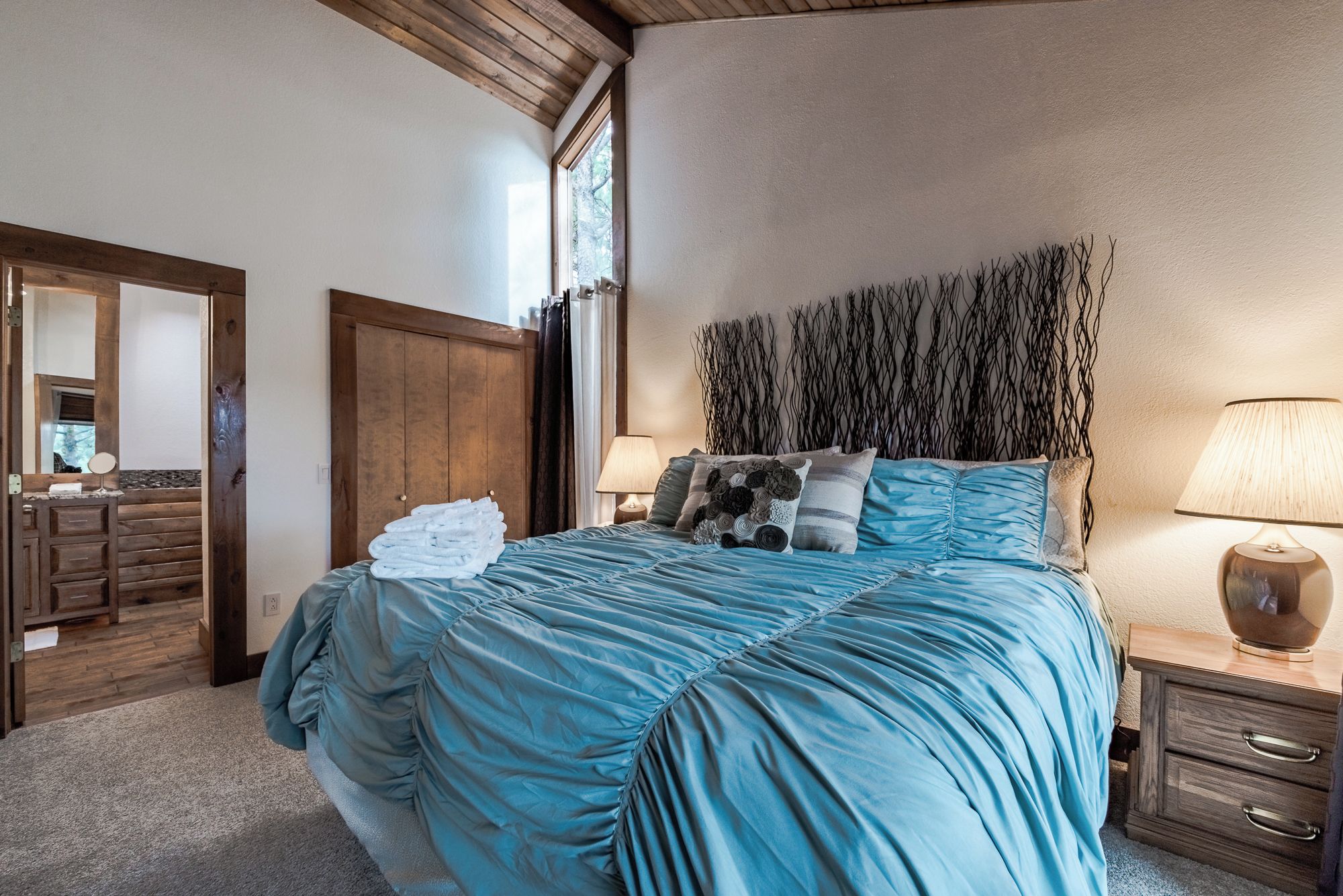 A bedroom with a large bed, wooden wardrobe, and a nightstand with a lamp.