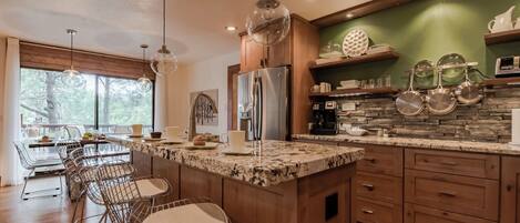 A modern kitchen with a granite countertop, stainless steel appliances, and a dining area with metal chairs.