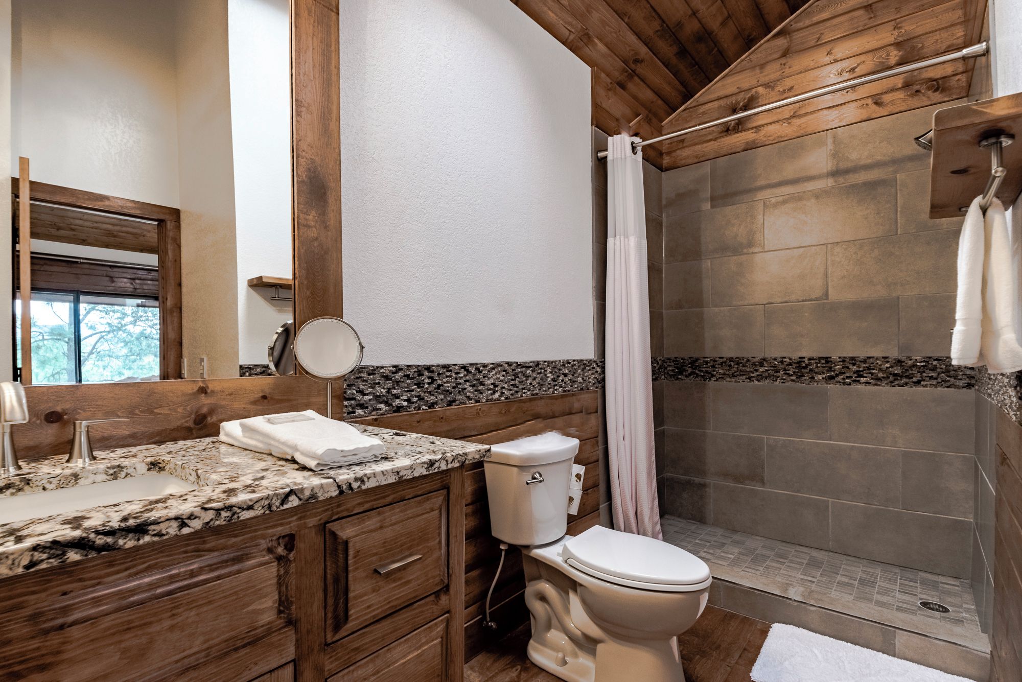 A bathroom with a wooden vanity, a toilet, a shower with a glass door, and a mirror.