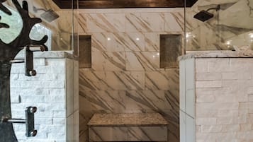 A bathroom with marble walls, a granite countertop, and a shower area.