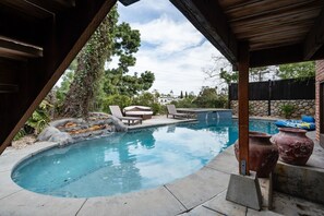 Una piscina con borde de piedra, sillas de descanso y una estructura de pérgola.