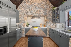 Una cocina con pared de piedra, una isla de madera y electrodomésticos modernos.