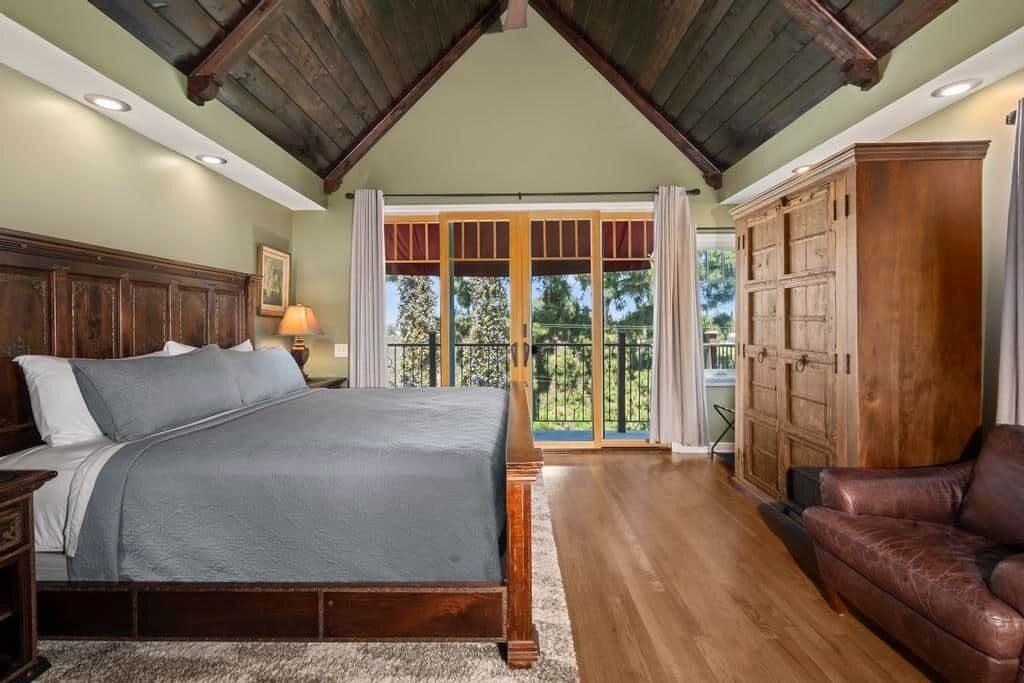 Un dormitorio con una cama grande, cabecera de madera, un aparador y un balcón con puertas de vidrio.