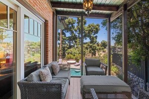Un patio techado con mobiliario de mimbre, una piscina y vistas a árboles y un edificio.