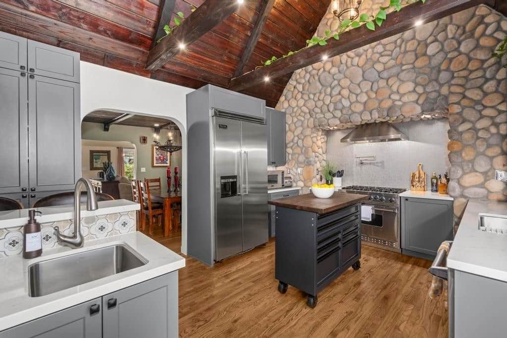A modern kitchen with a stone wall, stainless steel appliances, and a wooden ceiling.