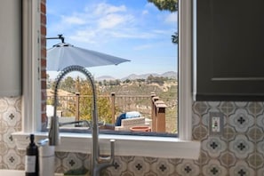 Una cocina con vista por la ventana a un balcón, mobiliario exterior y un paisaje montañoso.