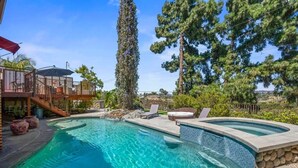 A swimming pool with a curved edge, a hot tub, and a deck area with outdoor furniture. - The Kensington Canyon Estate | Celebrity Vacation Homes (San Diego)