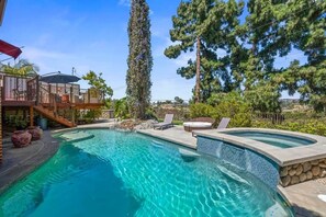 A swimming pool with a curved edge, a hot tub, and a deck area with outdoor furniture.