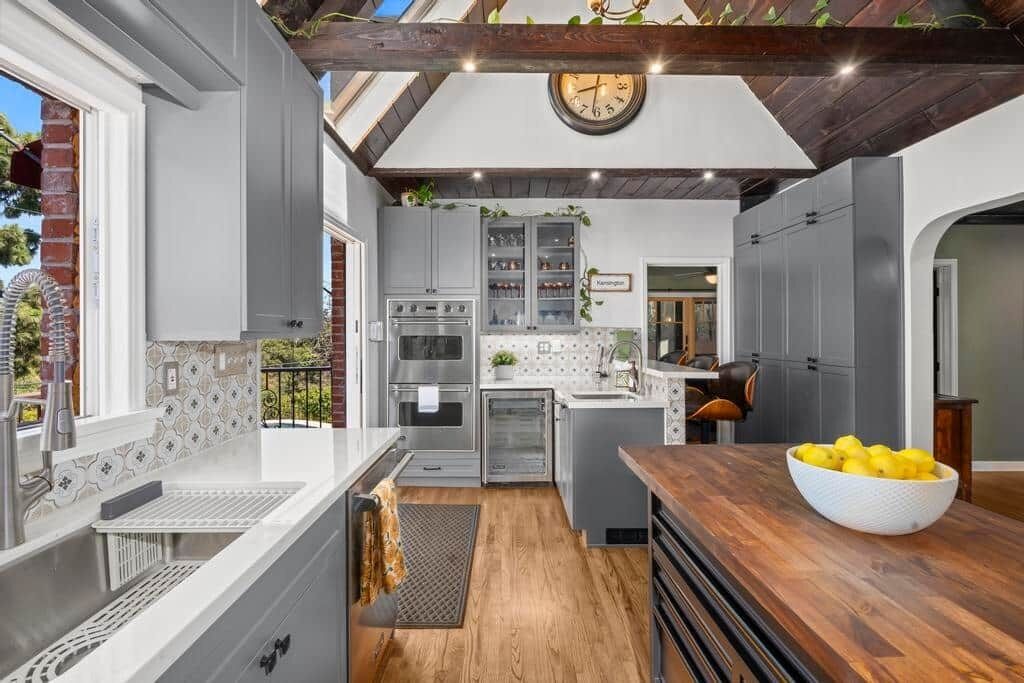 A modern kitchen with grey cabinets, a wooden countertop, and a clock on the wall.