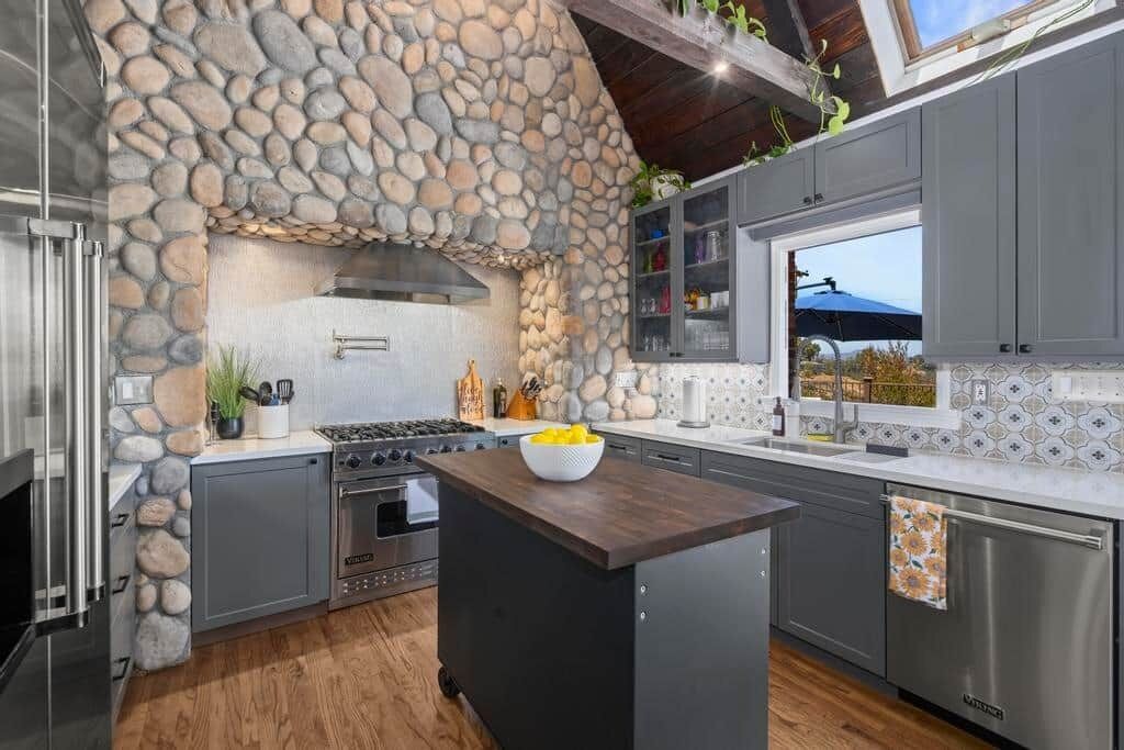 A modern kitchen with a stone accent wall, stainless steel appliances, and a view of the outdoors.