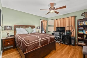 Un dormitorio con cama, escritorio, silla, estantería y ventilador de techo.