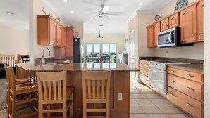 Una cocina con armarios de madera, una isla central con taburetes de bar, un ventilador de techo y vistas a un patio exterior.