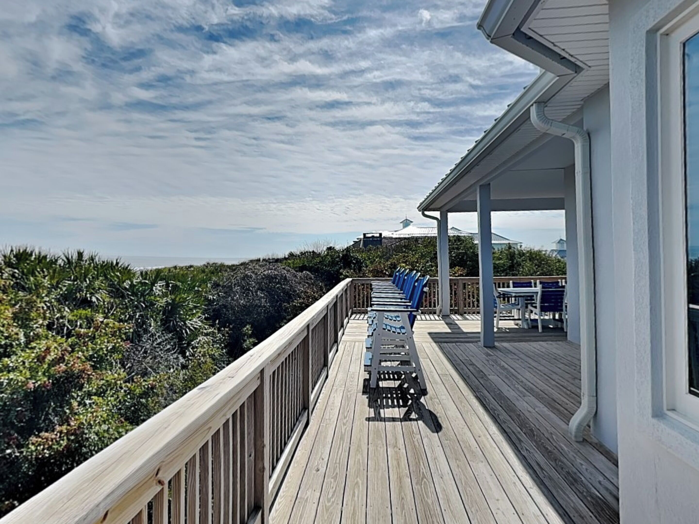A wooden deck with chairs and tables, overlooking a beach and ocean.