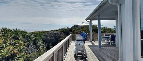 A wooden deck with chairs and tables, overlooking a beach and ocean.