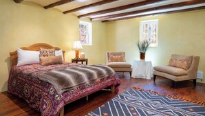 A bedroom with a large bed, two chairs, a small table with a lamp, and a window with curtains. - Casita Contenta by Kokopelli Property Management (Santa Fe)