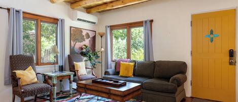 A cozy living room with a wooden ceiling, a sofa, a chair, a coffee table, and a colorful rug.