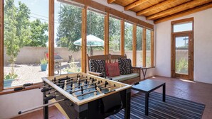 Ein Zimmer mit Tischfußballtisch, großen Fenstern, Holzboden und Blick ins Freie.