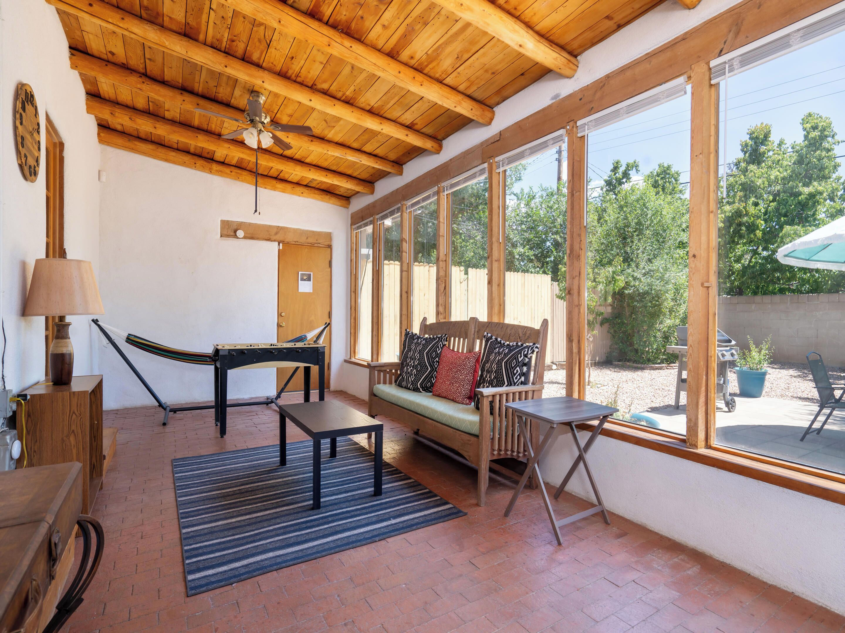 A spacious patio with a wooden ceiling, a hammock, a sofa with patterned cushions, and a table.