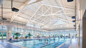 Une piscine intérieure avec des couloirs bien délimités, un plafond haut orné de motifs géométriques et de grandes fenêtres laissant entrer la lumière naturelle.