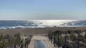 Un sentier qui longe la plage et mène à l’océan, sous un ciel dégagé.