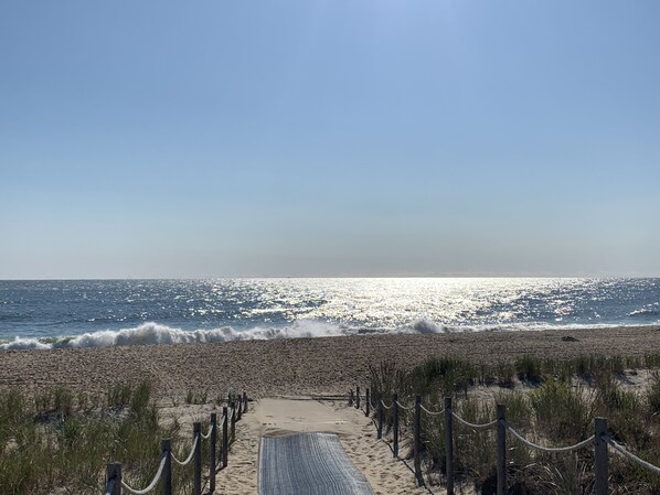 Un sentier qui longe la plage et mène à l’océan, sous un ciel dégagé.