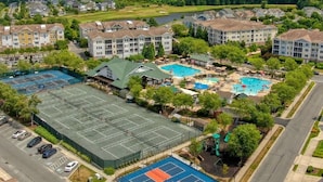 Vue aérienne d’un quartier résidentiel comprenant plusieurs immeubles d’appartements, un court de tennis et un complexe de piscines.