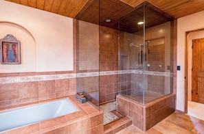 A modern bathroom with a glass-enclosed shower, a bathtub, and a wooden ceiling.