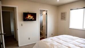 Ein Schlafzimmer mit Bett, Fernseher zeigt Kaminfeuer, Dusche und Fenster.