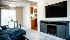 Ein Wohnzimmer mit einer Eckcouch, einem Couchtisch, einem Kamin und einem an der Wand befestigten Fernseher.