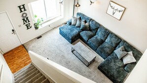 Ein modernes Wohnzimmer mit einem blauen Ecksofa, einem kleinen Couchtisch und einem Blumentopf am Fenster.