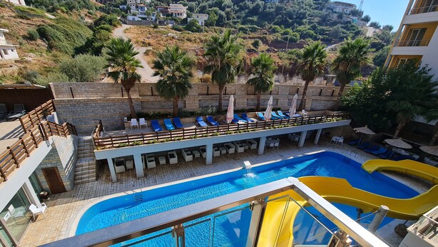 A swimming pool with a slide, lounge chairs, and a view of a hillside with buildings. - Holiday One Bedroom Sea View Apartment Vlore (Vlore)