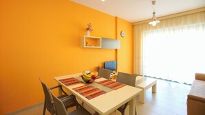 A dining area with a table set for two, a fruit bowl, and a television on the wall. - Holiday One Bedroom Sea View Apartment Vlore (Vlore)
