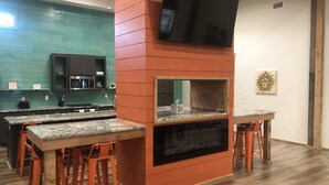 A modern kitchen with a built-in oven, a TV mounted on a red wall, and a wooden dining area with orange chairs. - Time For Livin…just a few steps from the Caddo River (Glenwood)