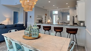 A modern kitchen with a central island, bar stools, and a dining table with chairs. - Three Palms by Distinctive Beach Rentals (Palm Coast)
