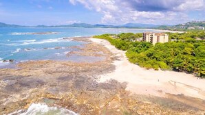 A coastal area with rocky shores, a sandy beach, and a building with multiple floors. - Villa Cerca Del Mar #6- 3BR House with Pool (Langosta)