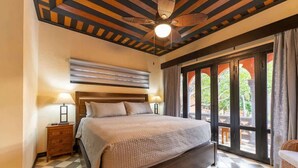 A bedroom with a large bed, two bedside tables with lamps, a ceiling fan, and a view through a glass door to an outdoor area. - Villa Cerca Del Mar #6- 3BR House with Pool (Langosta)